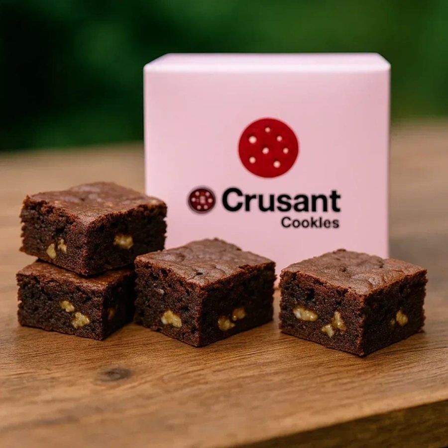 Walnut brownies cooling on a wooden board beside a pink Crusant box