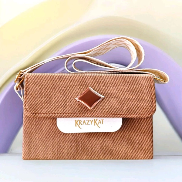 This beige KRAZY KAT sling bag features a brown diamond-shaped metallic accent on the flap.