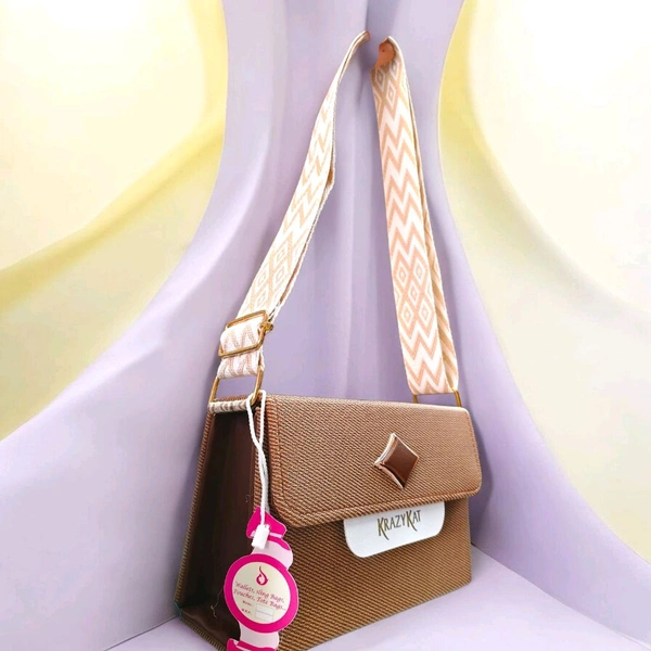 This beige KRAZY KAT sling bag features a brown diamond-shaped metallic accent on the flap.