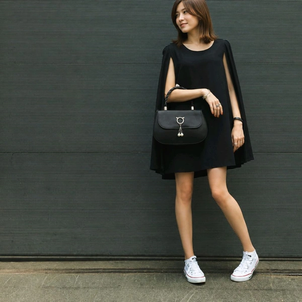 This black faux leather sling bag features a unique cat-ear hardware accent and a braided top handle.
