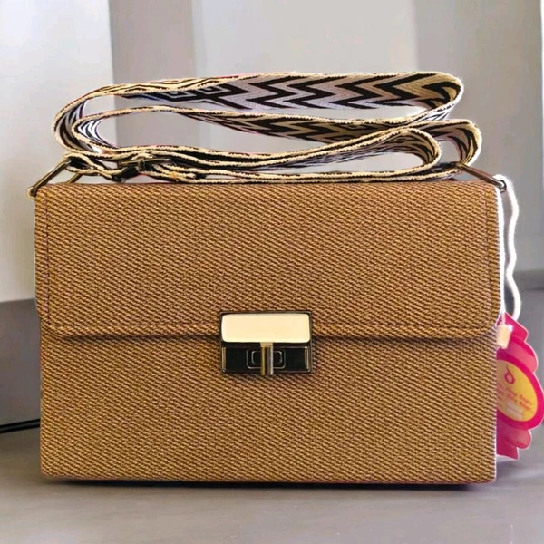 This textured brown crossbody bag features a patterned strap and a silver turn-lock closure.