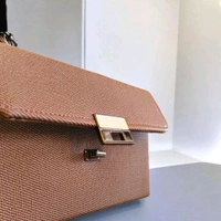 This textured brown crossbody bag features a patterned strap and a silver turn-lock closure.